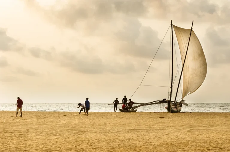 A wooden sailboat resting on the golden sands of Negombo beach, Sri Lanka, with gentle waves in the background