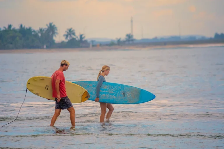 Couple walking along Arugam Bay beach with surfboards at sunrise, a top surfing spot in Sri Lanka