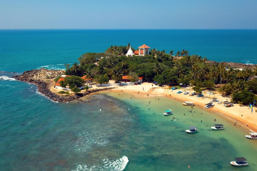 Wide view of Unawatuna Beach with golden sand, gentle waves, and palm trees lining the southern Sri Lankan shoreline